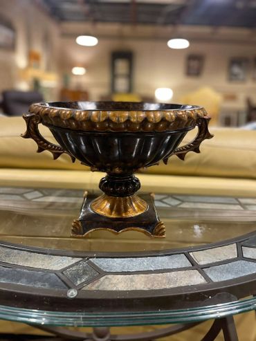 Ornate black and gold decorative bowl on glass table in cozy room.