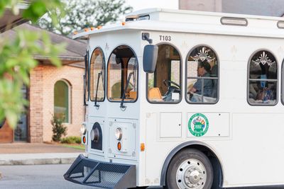 A white historical trolley with passengers inside on a street.