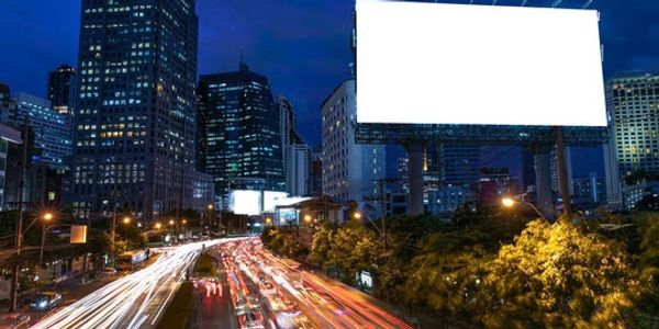 Busy city street at night with light trails and a large blank billboard.