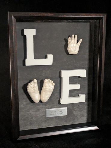 Baby hand and foot casting spelling LOVE in a dark shadow box with silver and black name plate