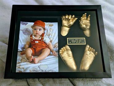 Shiny gold baby hand and foot casting displayed in a shadow box with photo and name plate