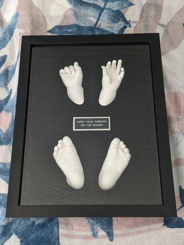 Clear coloured hand and foot casting of 12 month old in a black shadow box with black & silver plate