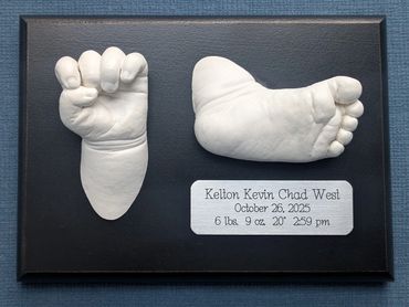 Baby hand and foot casting displayed on a black plaque.