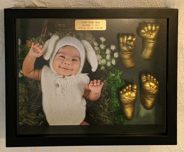 Golden baby hand and foot casting displayed in a black shadow box with photo and gold name plate