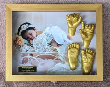 Gold baby hand and foot casting displayed in a gold shadow box with photo and name plate