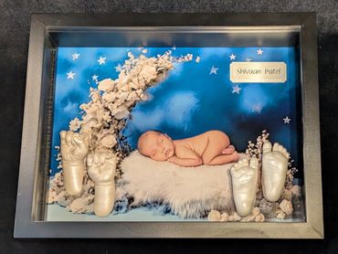 Black shadow box displaying a baby photo  with baby hand and foot casting