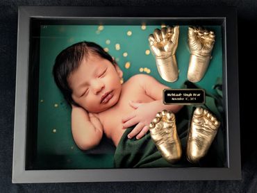 Shiny gold baby hand and foot casting displayed in a black shadow box with photo. 