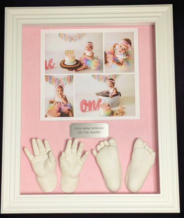 White stone coloured hand and foot casts  for a 1 year old girl displayed in a white shadow box.