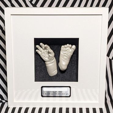 Pearl coloured baby hand and foot casting in a square shadow box with black and silver name plate