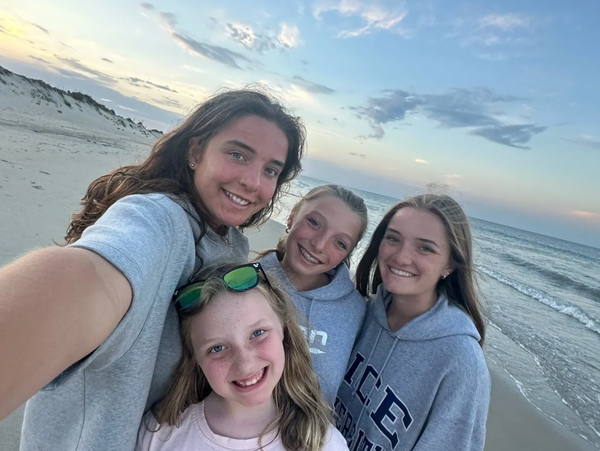 Four smiling girls taking a selfie on a beach at sunset.