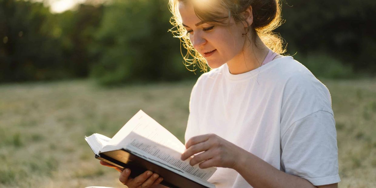 Woman reading a book outdoors in natural light.