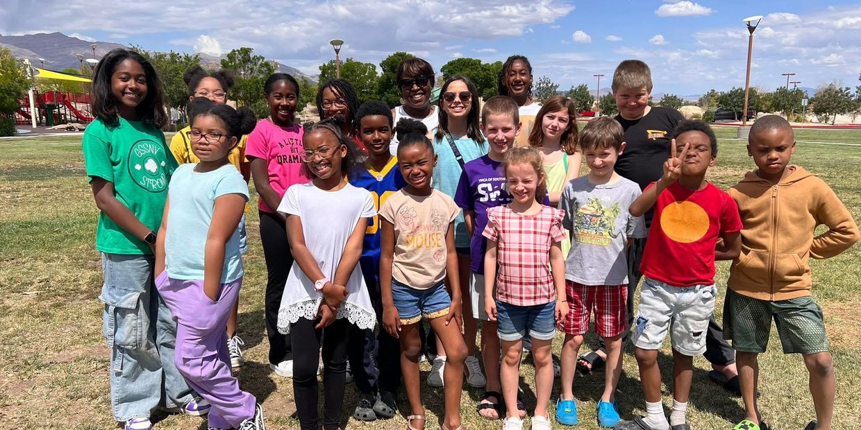 A diverse group of smiling children and two adults posing outdoors on a sunny day.