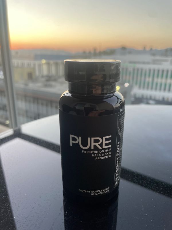 A black bottle of PURE dietary supplement for hair, nails, and skin on a reflective surface.