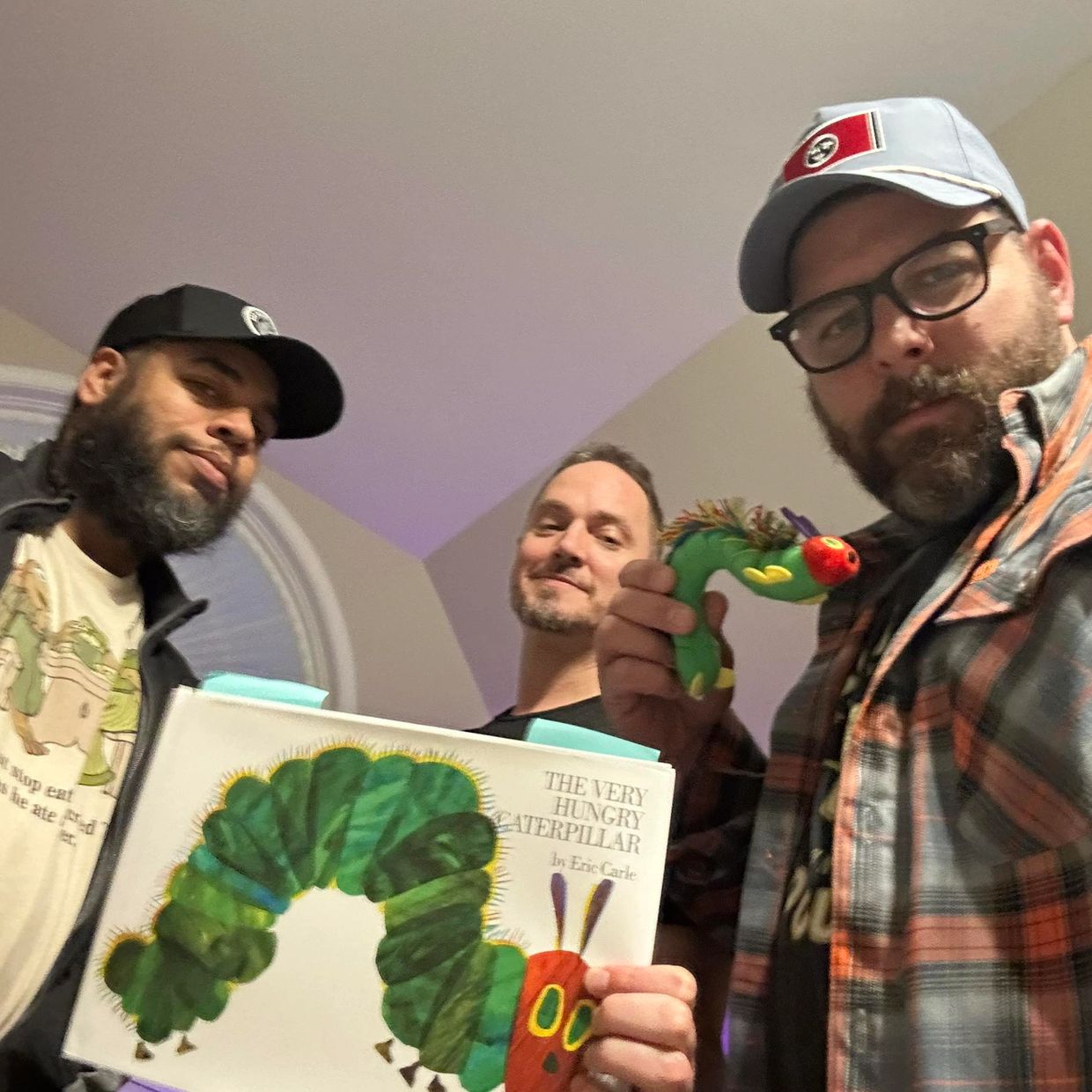 Three men posing with The Very Hungry Caterpillar book and toy.