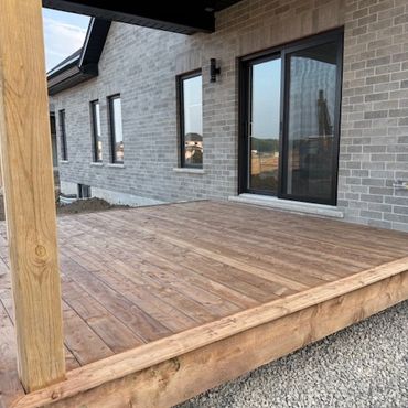 Newly constructed wooden deck next to a modern brick house with large windows.