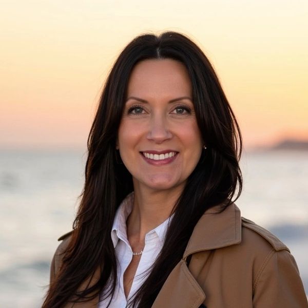 Smiling woman in a brown coat at the beach during sunset.
