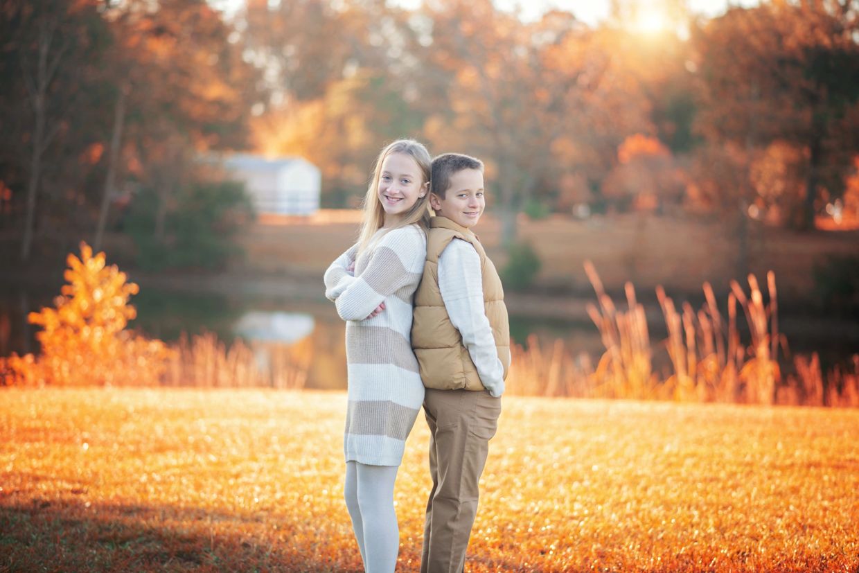 Two kids standing back-to-back outdoors in autumn with warm sunlight.