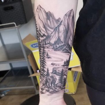 Tattoo of a mountain landscape with a river and a bear on a forearm.
