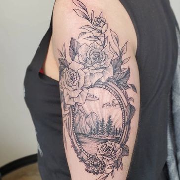 Black and gray tattoo of roses framing a nature scene on upper arm.