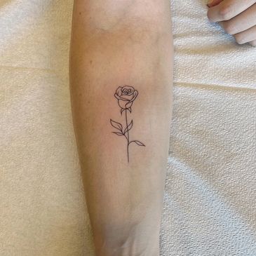 Minimalist single-line rose tattoo on forearm.