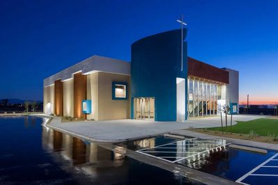 Modern church building illuminated at dusk with reflection on water.