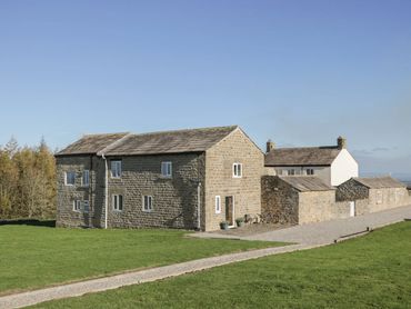 Stone farmhouse with adjacent buildings under clear blue sky.