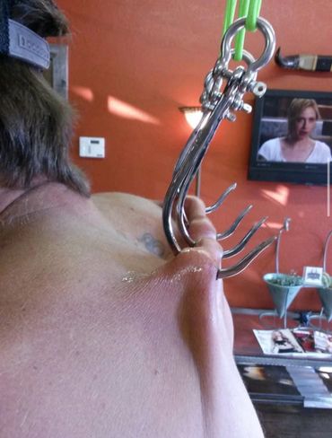 A person hanging by hooks pierced through their back skin.