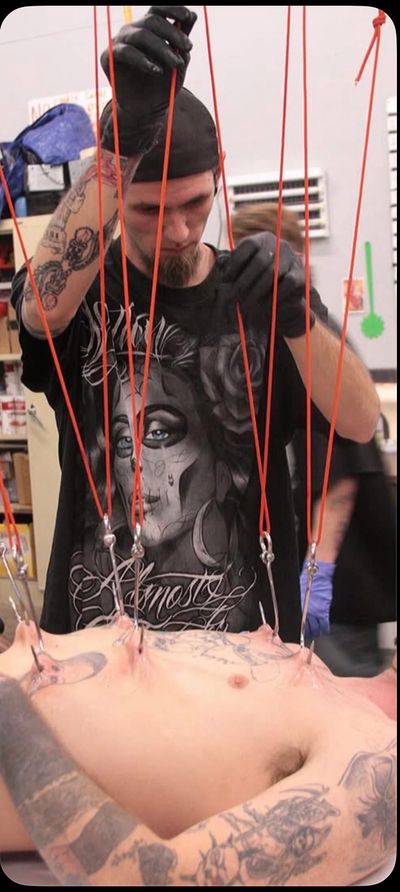 A tattooed man adjusting red cords attached to a person's chest in a studio.