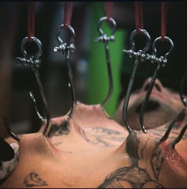 Person suspended by hooks piercing their skin in a body modification scene.