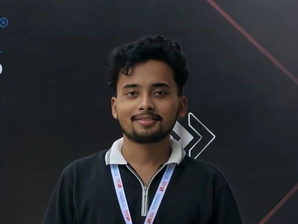 A man stands in front of a conference backdrop with floral decoration on the ground.