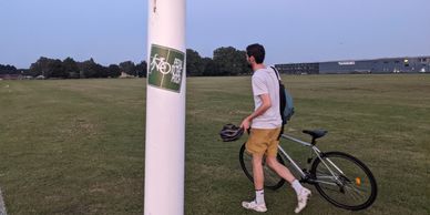 A Pedal to the Pitch sticker on a goalpost, with someone walking past holding their bike
