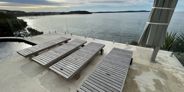 Tiled pool area with sun chairs and umbrella that overlooks the ocean.  Frameless glass balustrade.