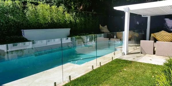 Backyard with tall hedge on fence line and cabana with grassed area next to pool.  
