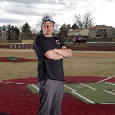 Baseball player standing on the field with arms crossed, wearing a cap and uniform.