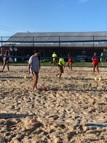 People playing volleyball on a sandy court under a clear sky.