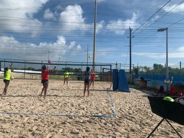 People playing volleyball on a sunny beach court under a blue sky.