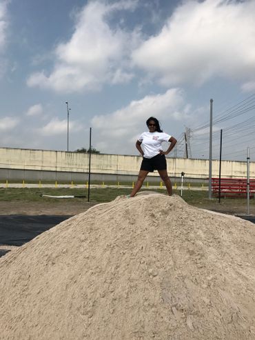 Person standing confidently atop a large dirt mound under a partly cloudy sky.