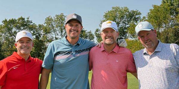 Four men posing together outdoors in golf attire.
