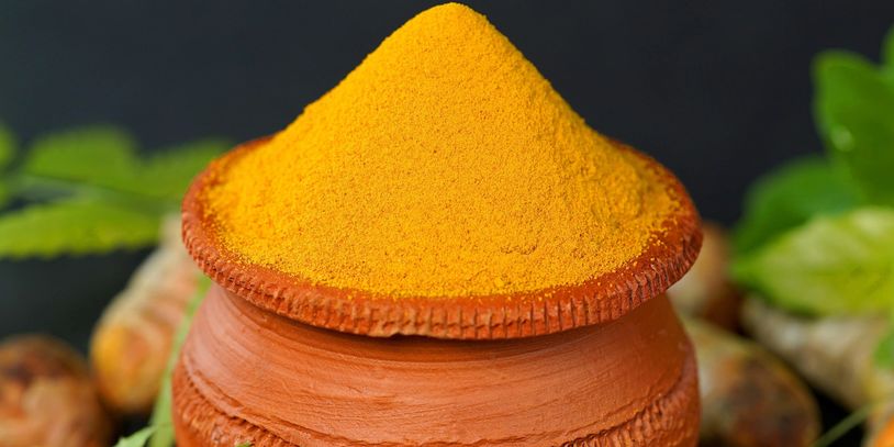 Bright yellow turmeric powder neatly piled in a traditional clay pot.