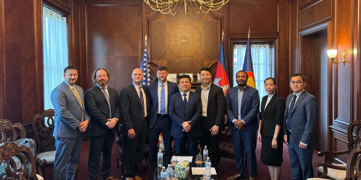 Group of professionals posing in an elegant wood-paneled room with flags.