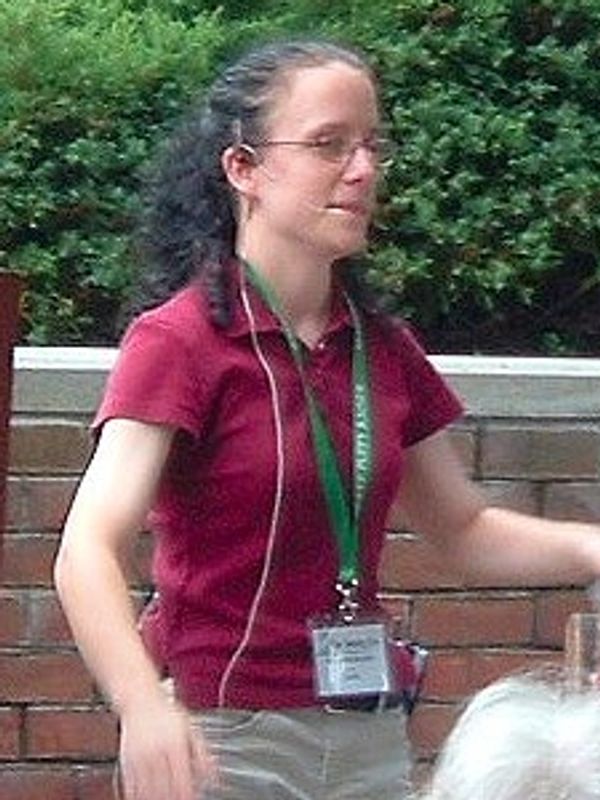 A close up shot of Heather giving a talk in an outdoor venue. Heather is wearing a wine coloured pol