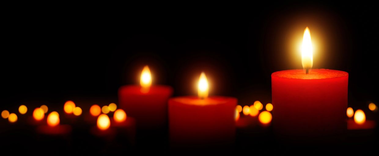 Three red candles burning in the dark with soft glowing bokeh lights.