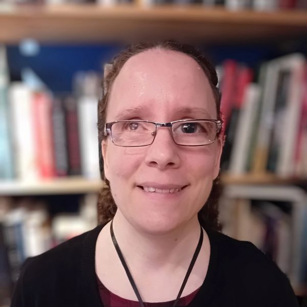 Photo of a headshot of Heather who is white with her brown curly hair pulled up. Heather is wearing 