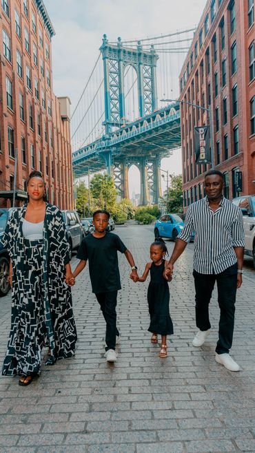 Stylish family walking hand-in-hand down the iconic cobblestone streets of DUMBO, Brooklyn with the Manhattan Bridge in the background. Captured during a family photoshoot in New York City, this image highlights the city's vibrant architecture and family bond in a trendy, urban setting. Perfect for showcasing family portrait sessions in NYC's most iconic locations.