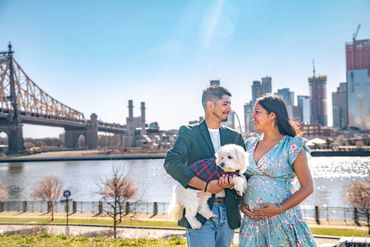 A joyful couple with their pet dog posing before a scenic urban backdrop featuring a bridge and sky