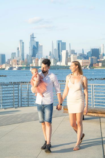 family walking together at the bay with skyline and ocean in the background with their baby  