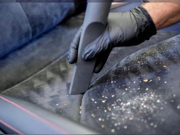Person vacuuming a car seat with dirt particles.