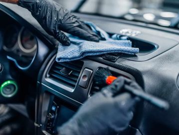 Person cleaning car dashboard with cloth and brush.
