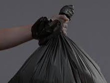 Hand holding a tied black garbage bag.