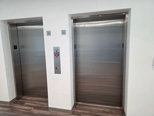 Two closed stainless steel elevator doors in a modern hallway.